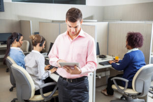 Young businessman using tablet computer while female colleagues working in background at call center