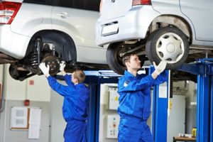 car mechanic inspecting car wheel and suspension detail of lifted automobile at repair service station